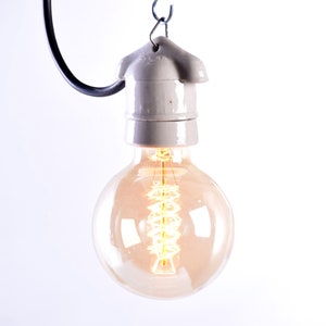 May include: A vintage-style, round light bulb with a warm, amber glow. The bulb features a visible filament and is suspended from a gray ceramic socket and a black wire. The design evokes a classic, industrial aesthetic.