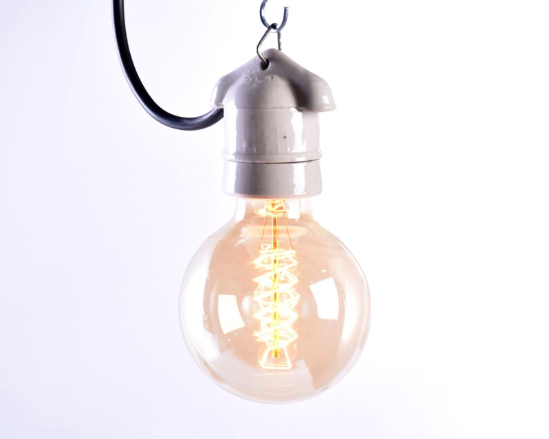 May include: A vintage-style, round light bulb with a warm, amber glow. The bulb features a visible filament and is suspended from a gray ceramic socket and a black wire. The design evokes a classic, industrial aesthetic.