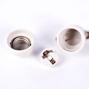 May include: Three-piece, off-white ceramic light fixture components. The components include a socket with a metal interior, a threaded base, and a small, round piece with electrical contacts. The base has the numbers "16" and "38" printed on it.