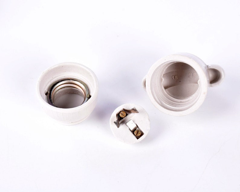 May include: Three-piece, off-white ceramic light fixture components. The components include a socket with a metal interior, a threaded base, and a small, round piece with electrical contacts. The base has the numbers "16" and "38" printed on it.
