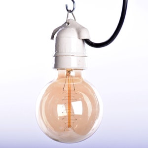 May include: A vintage-style light bulb with a warm, amber glow. The bulb is round and suspended from a white ceramic socket and a black wire. The filament is visible inside the glass, creating a classic, industrial aesthetic.