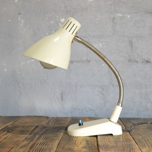 K&ouml;nnte beinhalten: Eine wei&szlig;e Vintage-Tischlampe mit flexiblem Arm und wei&szlig;em Schalter. Die Lampe hat einen wei&szlig;en Metallschirm mit einem kleinen Loch oben.