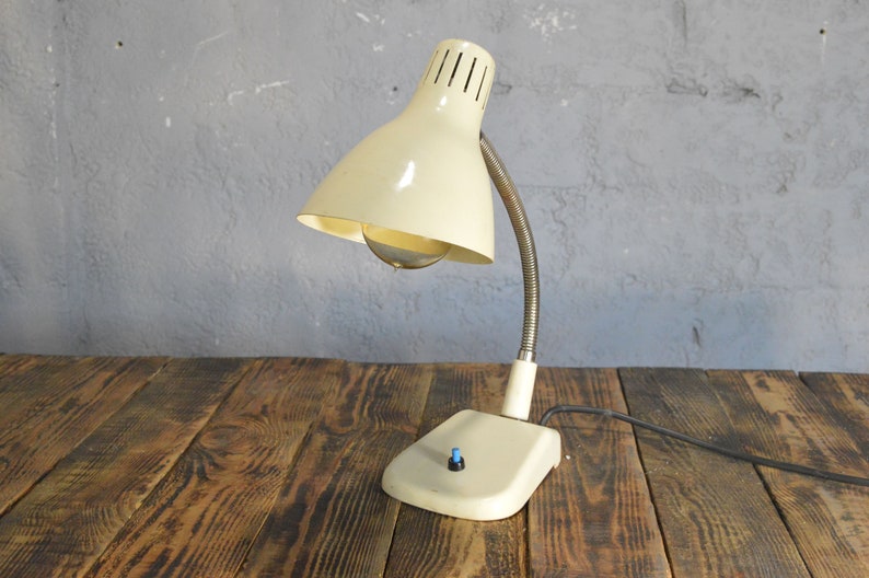 K&ouml;nnte beinhalten: Eine wei&szlig;e Vintage-Tischlampe mit flexiblem Arm und wei&szlig;em Schirm. Die Lampe hat einen runden Sockel mit einem blauen Schalter.
