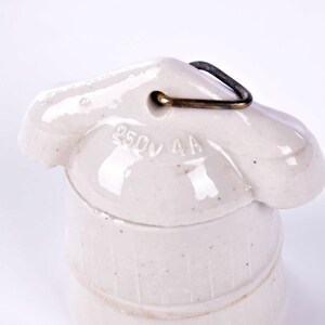 May include: A cream-colored ceramic electrical insulator with a metal loop. The insulator has the text "250V 4A" imprinted on its surface. The design features a rounded top and a cylindrical base, with vertical ridges.