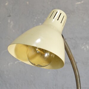 K&ouml;nnte beinhalten: Eine vintage wei&szlig;e Schreibtischlampe mit einem flexiblen Metallarm und einem wei&szlig;en Schirm mit einer Gl&uuml;hbirne im Inneren.