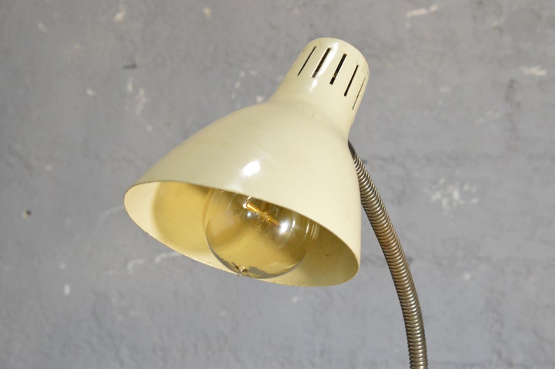 K&ouml;nnte beinhalten: Eine vintage wei&szlig;e Schreibtischlampe mit einem flexiblen Metallarm und einem wei&szlig;en Schirm mit einer Gl&uuml;hbirne im Inneren.