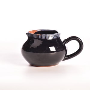 May include: A small, black ceramic creamer with a blue and white rim. The creamer has a rounded body and a handle.