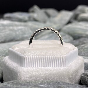 May include: A silver band with a row of small diamonds set in a pave setting.