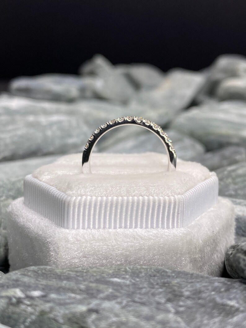 May include: A silver band with a row of small diamonds set in a pave setting.