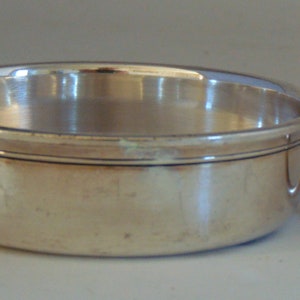 May include: A silver cup with a leaf-shaped handle. The cup is round and has a smooth, polished surface.