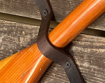 May include: A wooden paddle with a leather strap and screws for hanging on a wall.