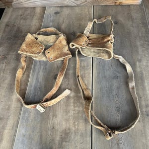 May include: Two brown leather straps with buckles, possibly used for climbing or securing objects.