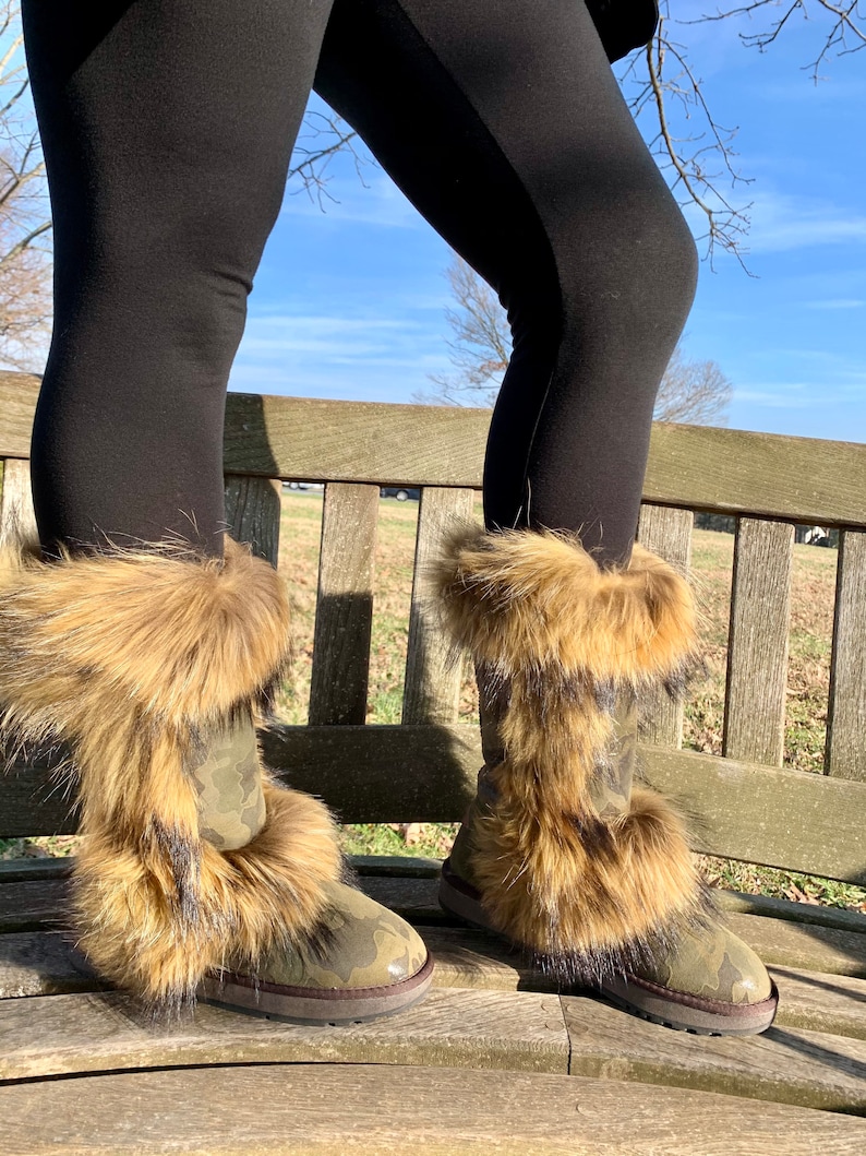 Peut inclure: Une paire de bottes de camouflage brun et vert avec un &eacute;pais revers en fourrure. Les bottes sont pos&eacute;es sur un banc en bois.