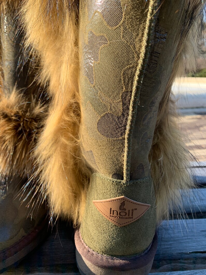 Peut inclure: Bottines en daim vert avec un motif camouflage et une bordure en fausse fourrure. Les bottes ont une &eacute;tiquette en cuir marron avec le texte "Inolir Luxury Reinvented".
