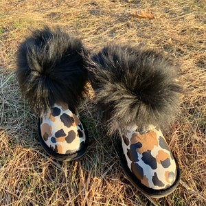 Puede incluir: Un par de botas de piel negra con un patrón de camuflaje marrón y blanco.