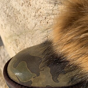 Peut inclure: Gros plan sur une botte de camouflage vert avec une bordure en fourrure brune. La botte a une semelle en caoutchouc brune.