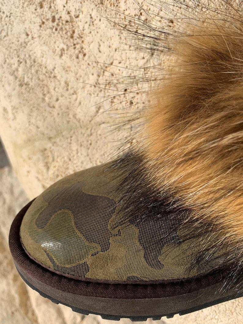 Peut inclure: Gros plan sur une botte de camouflage vert avec une bordure en fourrure brune. La botte a une semelle en caoutchouc brune.