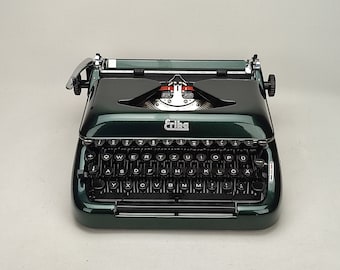 May include: A green Erika brand typewriter with a black keyboard and silver accents. The typewriter has a carriage return lever and a paper roller.