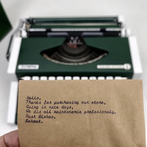 May include: A vintage green Olympia typewriter with white accents. A handwritten note in black ink is held in front of the typewriter. The note reads: "Hello, Thanks for purchasing our store, Using in nice days, We did all maintenance profesionaly, Best Wishes, Mehmet."