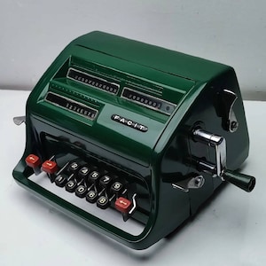 Op de afbeelding: Een groene vintage Facit-rekenmachine met een handkrans en een rij met nummertoetsen. De machine heeft een displayvenster met de nummers 000000003.
