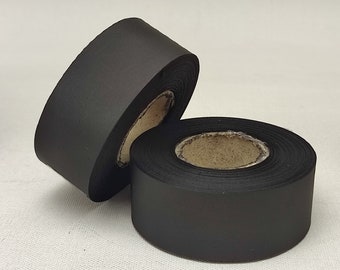 May include: Two rolls of black satin ribbon are displayed against a white background. The ribbon is tightly wound around cardboard cores. The satin has a smooth, matte finish, and the rolls are positioned to show the ribbon's texture.