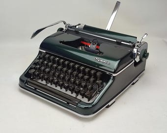 Puede incluir: Una máquina de escribir Olympia vintage de color verde con un teclado negro y detalles plateados. La máquina de escribir tiene una palanca de retorno de carro y una palanca de liberación de papel.