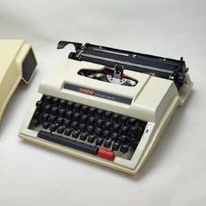 May include: A white Brother Deluxe 750TR typewriter with a black keyboard and a red repeat spacer button.