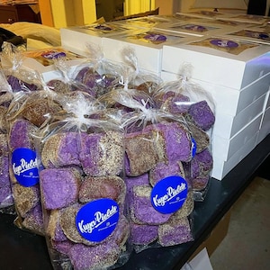 May include: A close-up of several bags filled with purple and brown ube bread. The bags are labeled "Kuya Piele's" and are stacked on a table. The bread is a popular Filipino dessert.