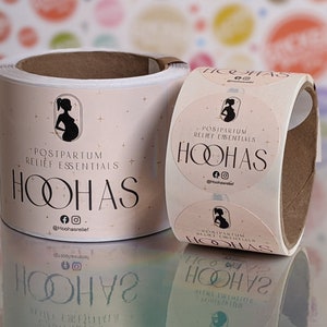 May include: Roll of round stickers with a pink background and a black silhouette of a pregnant woman. The text "POSTPARTUM RELIEF ESSENTIALS HOOHAS" is printed in black on the stickers. The social media handle "@hoohasrelief" is printed below the text.