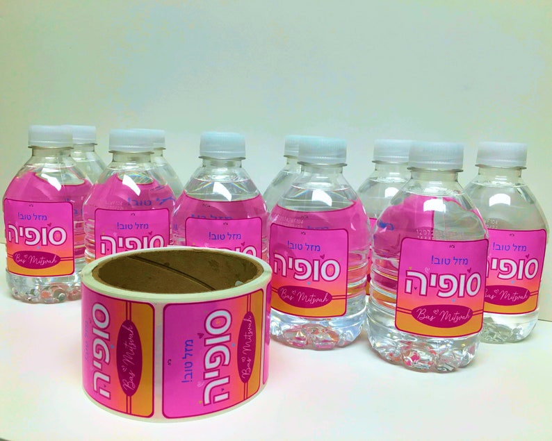 May include: A roll of pink and orange stickers with the Hebrew text "Mazal Tov Sophia" and the English text "Bar Mitzvah" on them. The stickers are designed for water bottles.