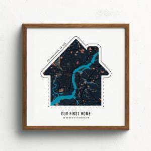 May include: A white framed print with a house-shaped design featuring a map of Philadelphia, Pennsylvania. The text "Our First Home" is below the map with the coordinates "39.9526° N 75.1652° W".