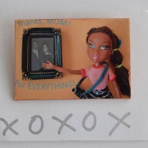 Puede incluir: Una tarjeta con una imagen de una muñeca sosteniendo una foto enmarcada. La tarjeta dice "¡Gracias, MAMÁ! ¡Por TODO!" y "XOXO" en letras grises.
