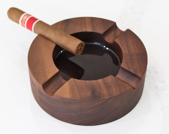 May include: A dark brown wooden cigar ashtray with a deep well and a cigar resting on the rim.