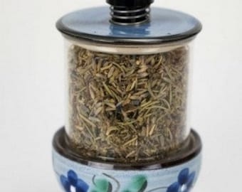 May include: A blue and white ceramic spice grinder with a black plastic top and a spring mechanism. The grinder is filled with dried herbs.