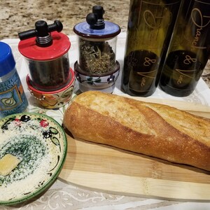 May include: A wooden cutting board with a loaf of bread, a small plate with a slice of cheese, two ceramic spice grinders, and two bottles of wine labeled "Branch & Vine, Inc."
