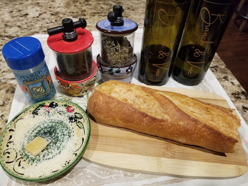 May include: A wooden cutting board with a loaf of bread, a small plate with a slice of cheese, two ceramic spice grinders, and two bottles of wine labeled "Branch & Vine, Inc."