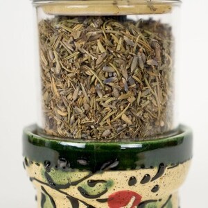 May include: A ceramic herb grinder with a green and white floral design. The grinder has a clear glass jar filled with dried herbs.