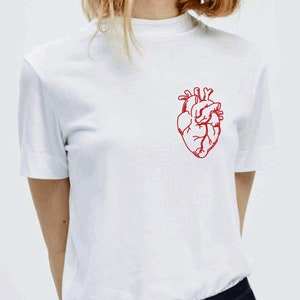 May include: White t-shirt with a red anatomical heart graphic on the front.
