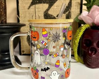 May include: A clear glass mug with a bamboo lid and a straw. The mug has a Halloween theme with images of pumpkins, ghosts, bats, candy corn, and lollipops.