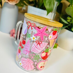 Peut inclure: Mug en verre transparent avec couvercle et paille en bambou, d&eacute;cor&eacute; d'illustrations roses et rouges sur le th&egrave;me de l'&eacute;t&eacute;. Le motif comprend une &eacute;toile de mer, des coquillages, des cornets de glace, des cerises et des fraises.