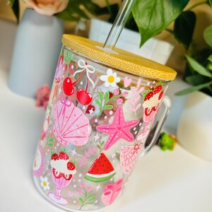 Peut inclure: Un gobelet en verre transparent avec un couvercle en bambou et une paille en verre. Le gobelet est d&eacute;cor&eacute; d'illustrations roses et rouges sur le th&egrave;me de l'&eacute;t&eacute;, notamment des cerises, un coquillage, une &eacute;toile de mer et une tranche de past&egrave;que.