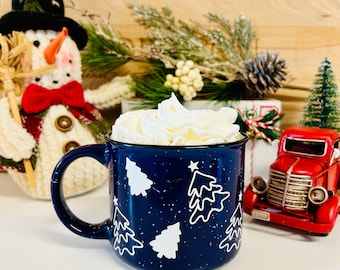 May include: A blue ceramic mug with white Christmas trees and white speckles. The mug is filled with whipped cream.