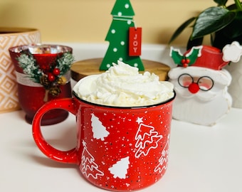May include: Red ceramic mug with white Christmas tree designs and a white rim. The mug is filled with a hot drink topped with whipped cream.