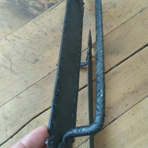 May include: Black metal door handle with a decorative design. The handle is attached to a metal plate with a decorative edge.