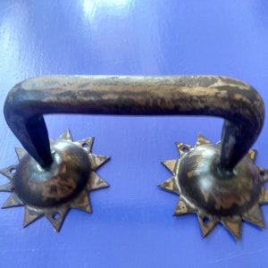 Può includere: Una maniglia per porta in metallo nero rustico con un design a forma di stella su ciascuna estremità. La maniglia è curva e presenta una finitura usurata e invecchiata.