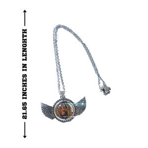 Puede incluir: Collar de cadena de plata con un colgante que presenta una foto de una persona con rastas y alas adornadas con diamantes de imitaci&oacute;n. El collar mide 55 cm de largo.