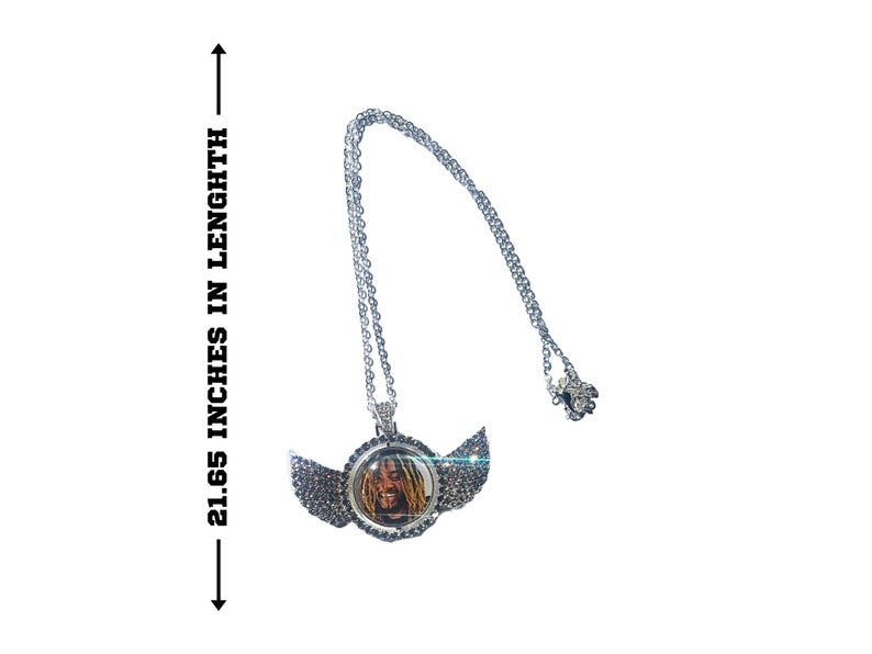 Puede incluir: Collar de cadena de plata con un colgante que presenta una foto de una persona con rastas y alas adornadas con diamantes de imitaci&oacute;n. El collar mide 55 cm de largo.