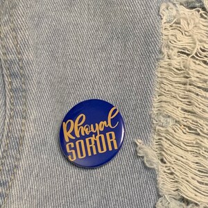 May include: A blue button with the words "Royal Soror" written in gold lettering.