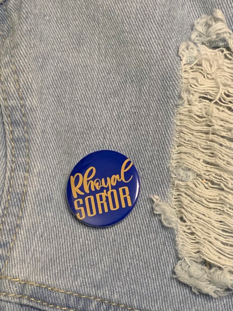 May include: A blue button with the words "Royal Soror" written in gold lettering.