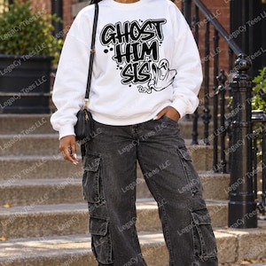 May include: A white long-sleeve crewneck sweatshirt featuring the black text GHOST HIM SIS and a graphic of a ghost. The sweatshirt is paired with dark gray denim cargo pants that have large side pockets and black and white athletic sneakers.